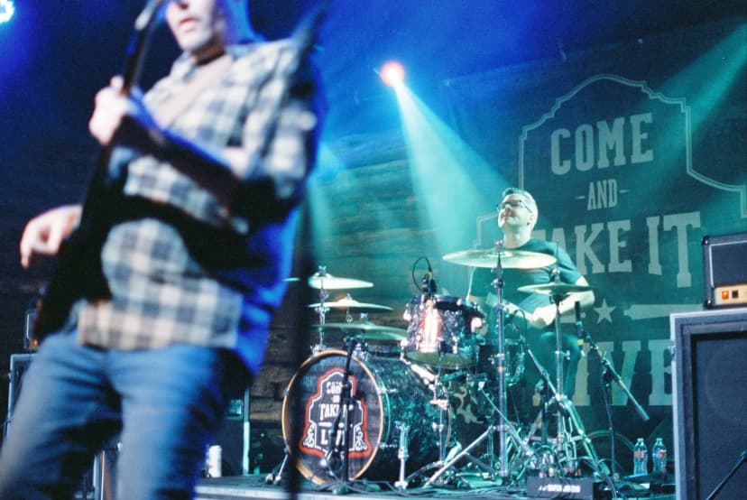 a man is playing a guitar on a stage in front of a drum set .