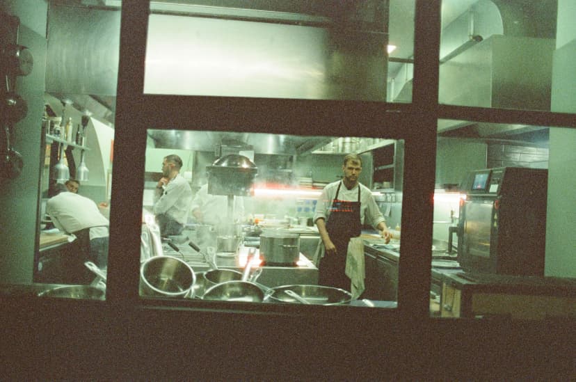 a man in an apron is standing in a kitchen in front of a window .