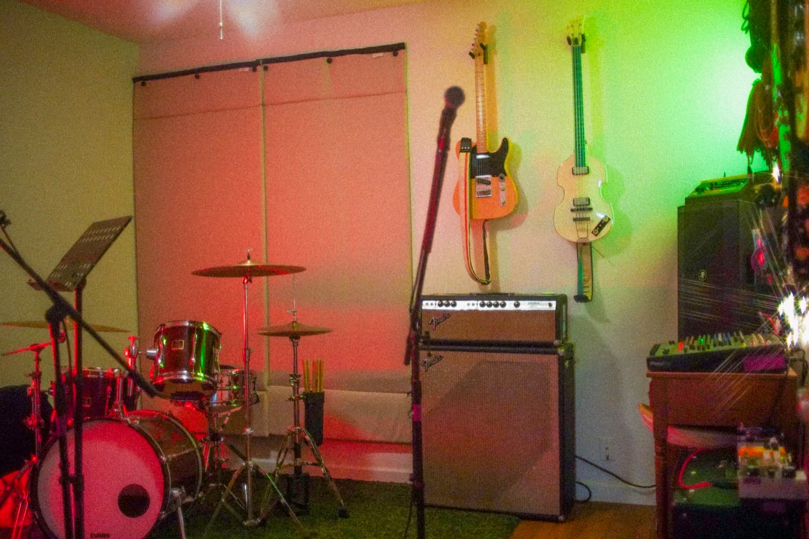 Band practice room with drum kit, mics, guitars on the wall, and a Fender bass rig